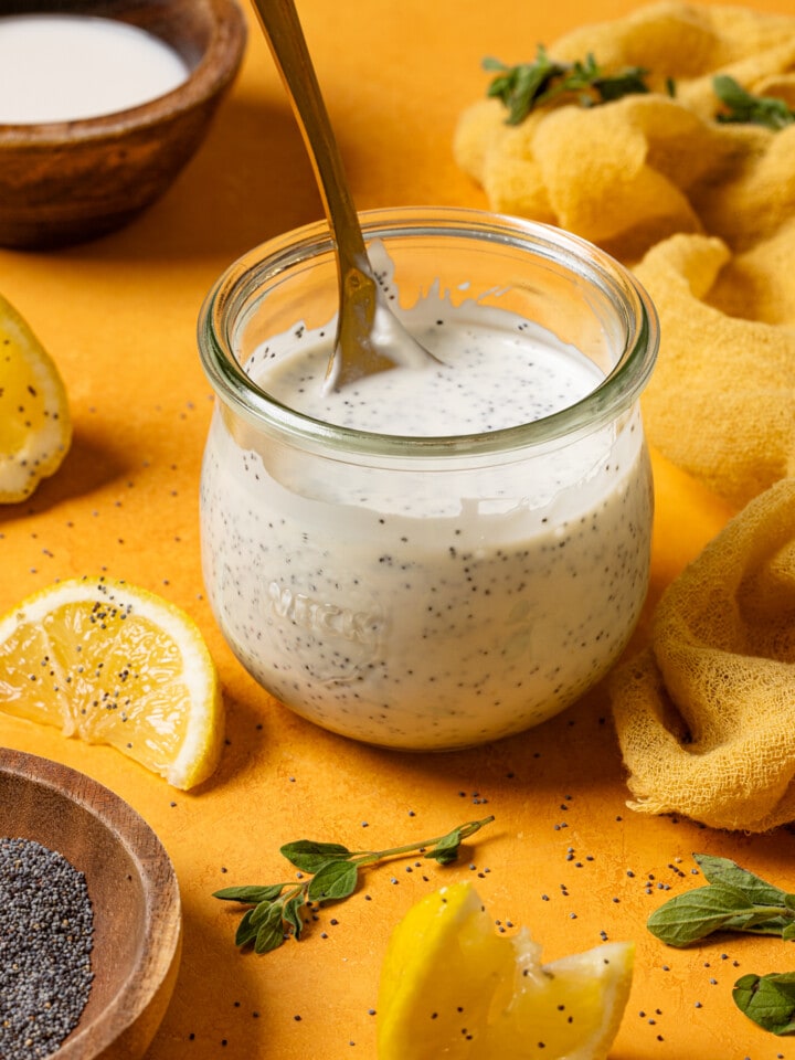 Lemon poppyseed dressing in a mason jar with a spoon and lemon wedges.