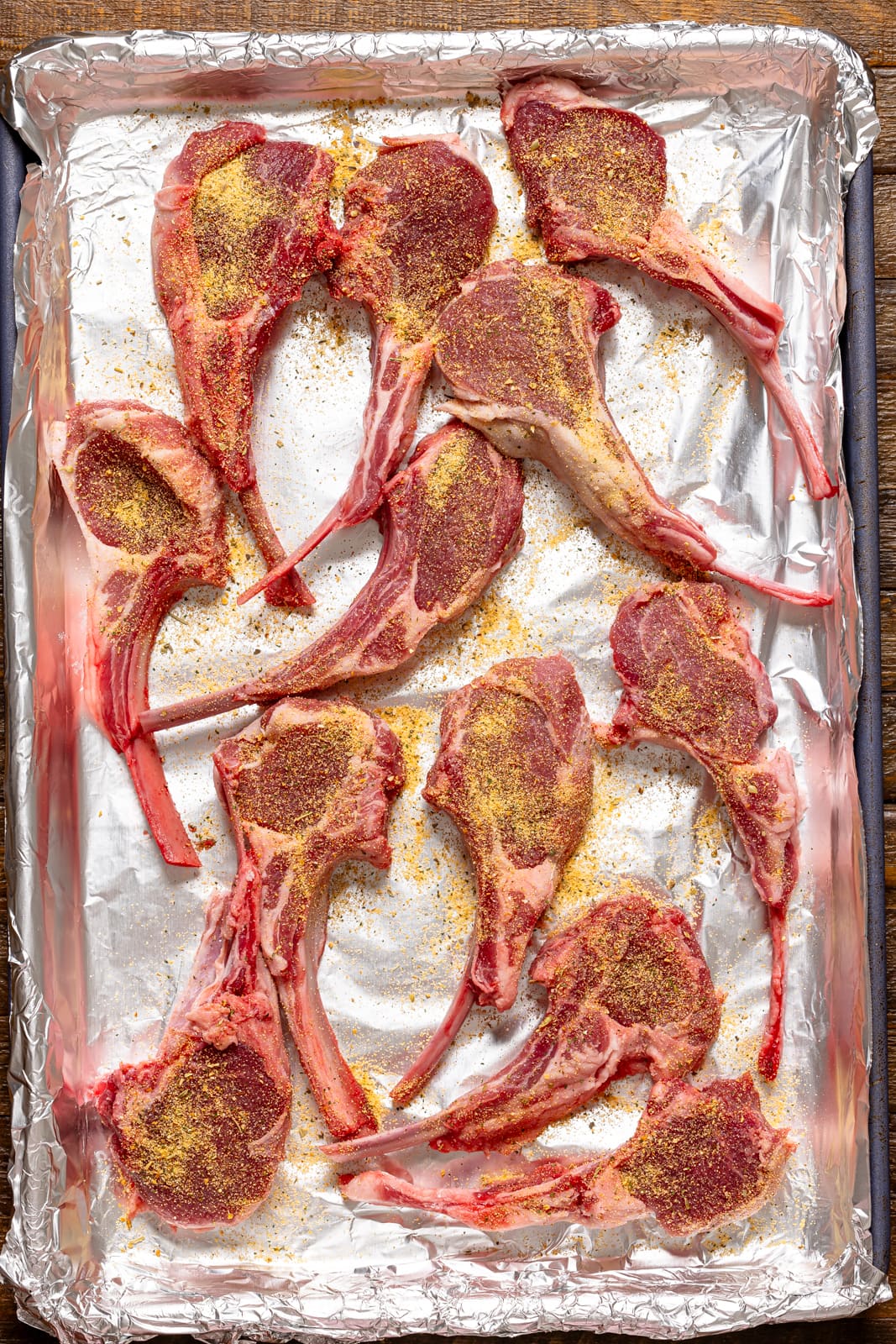 Lamb chops lined on a baking sheet with foil paper and seasoned. 