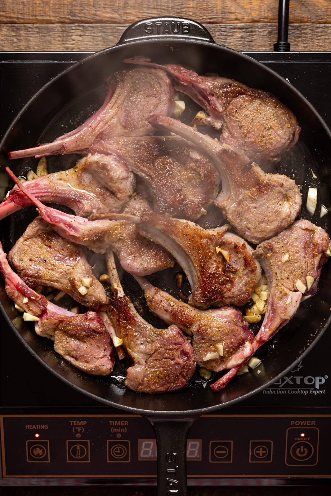 Lamb chops being seared in a black skillet. 