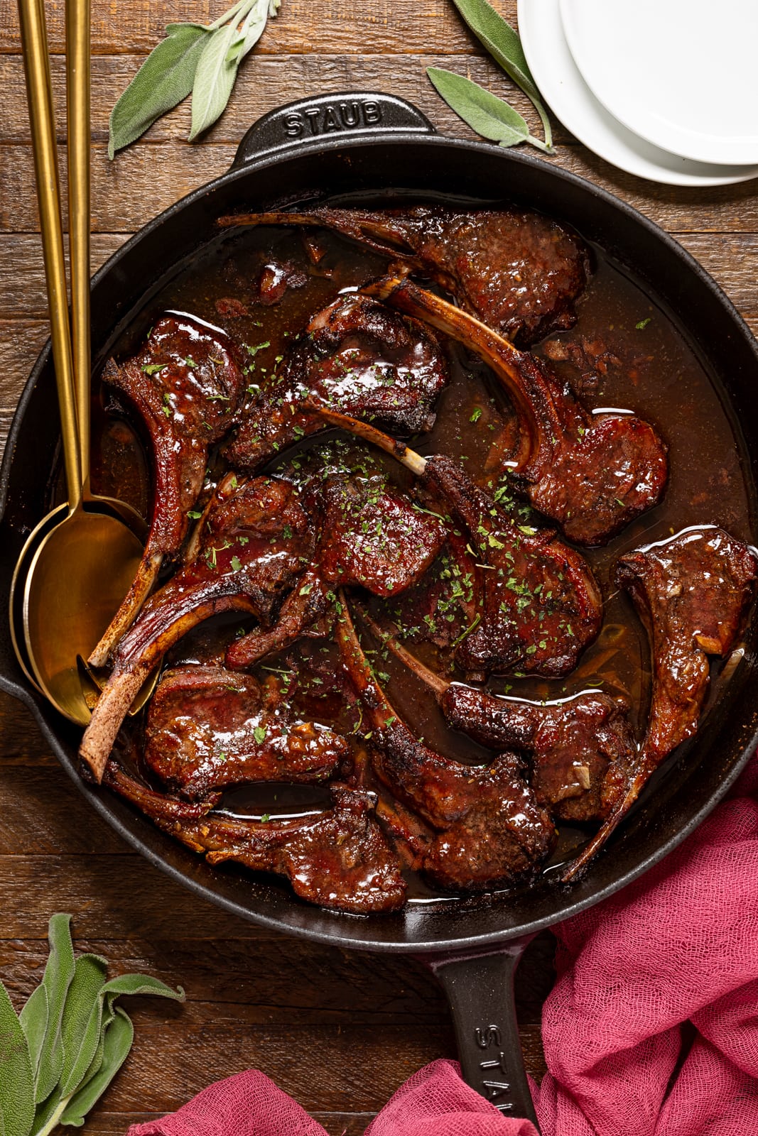 Cooked lamb chops in a black skillet with gold serving spoons.