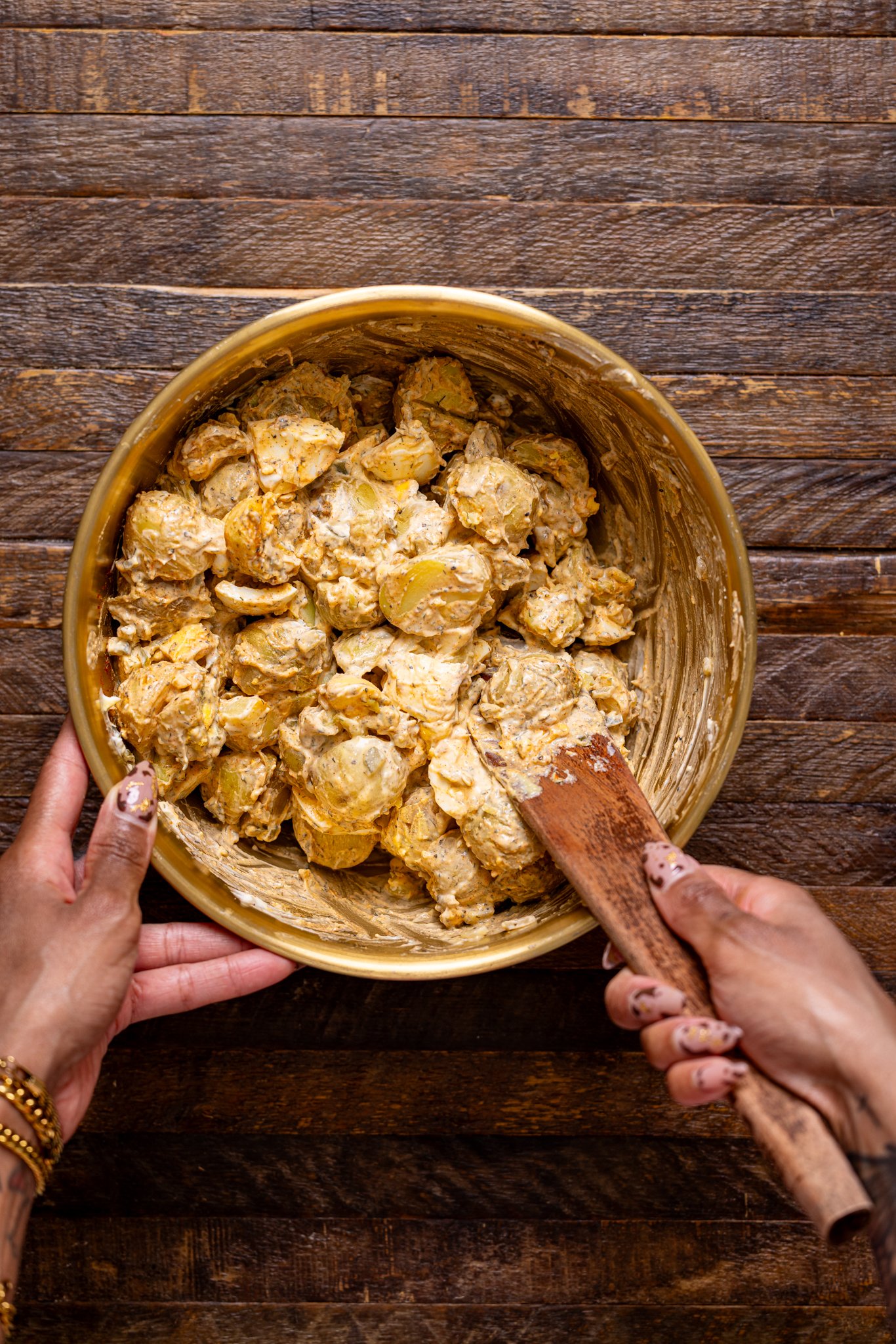 Potato salad ingredients being mixed together by woman hands.