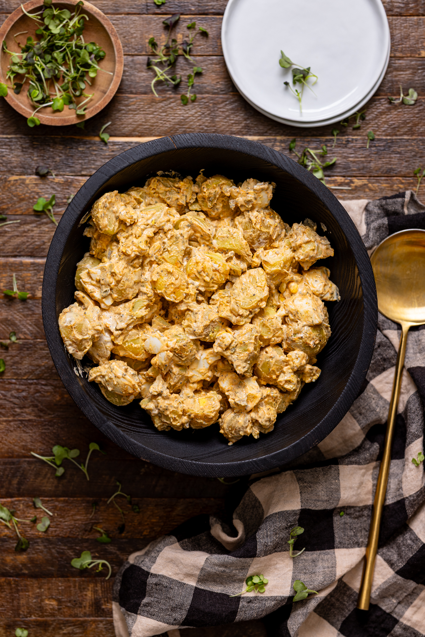 My Fave Southern Potato Salad Recipe in a black bowl with a gold spoon and plates.