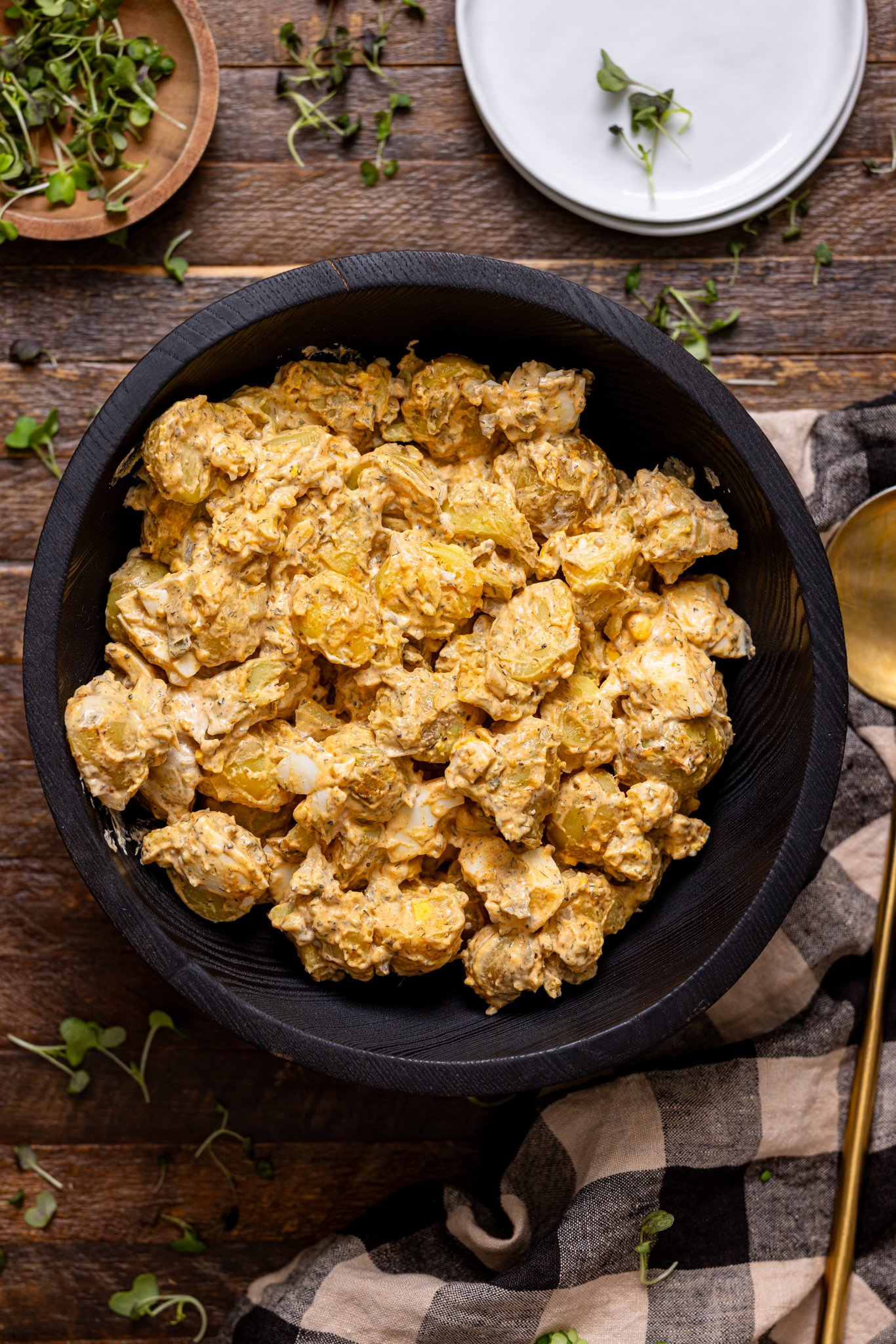 My Fave Southern Potato Salad Recipe in a black bowl with a gold spoon on a brown wood table.