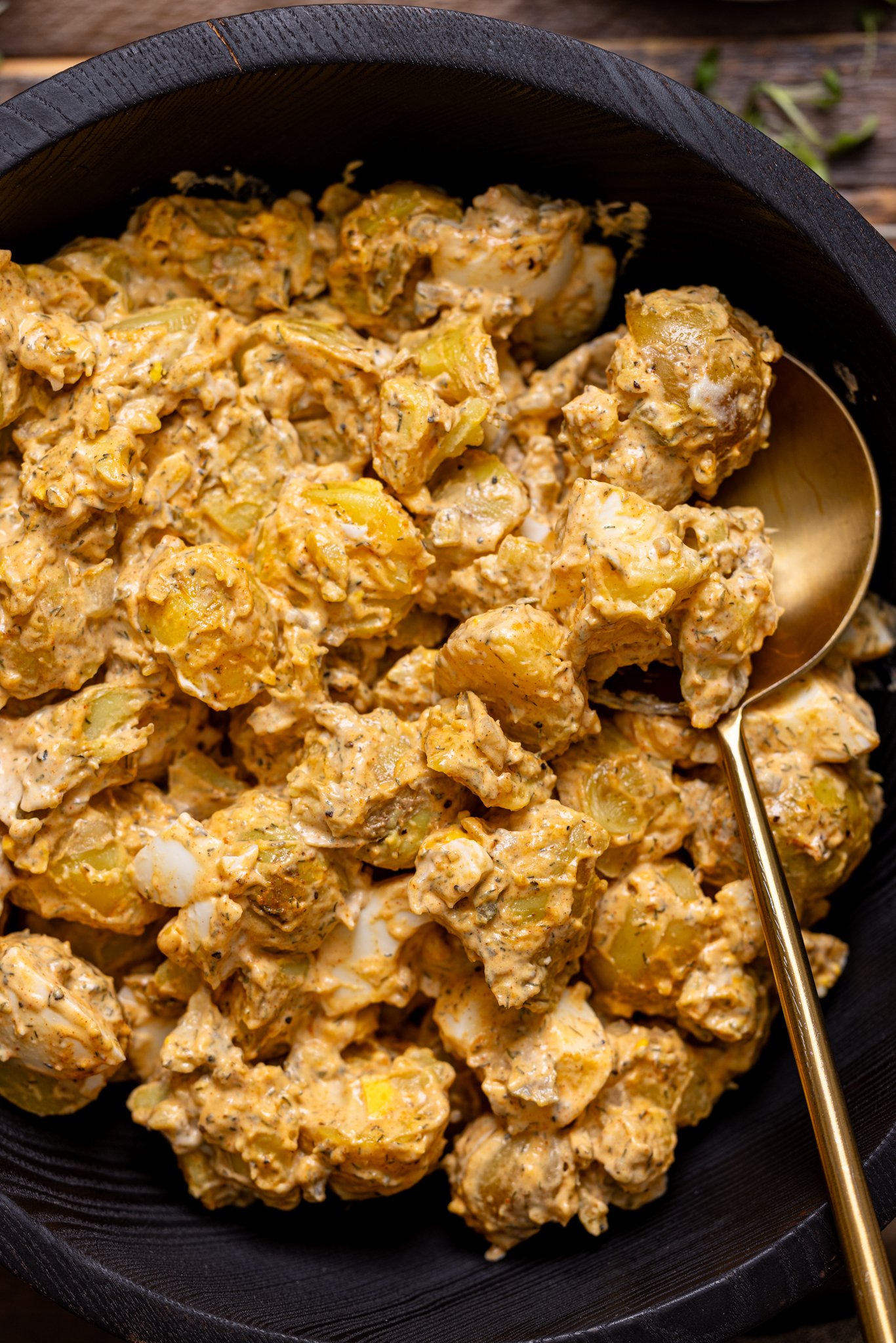 Up close shot of potato salad in a black bowl with a spoon.