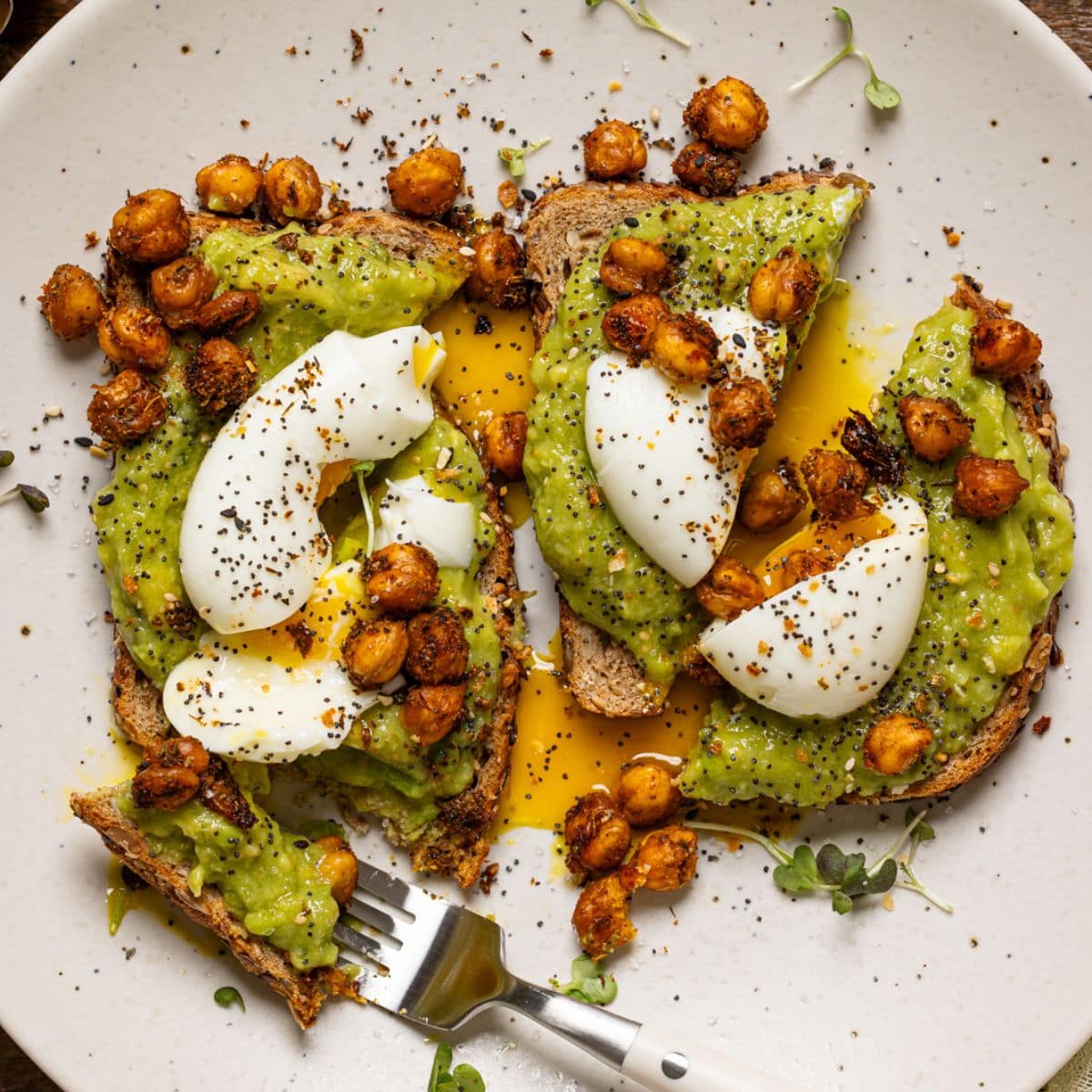 Avocado toast with a fork on a white plate.