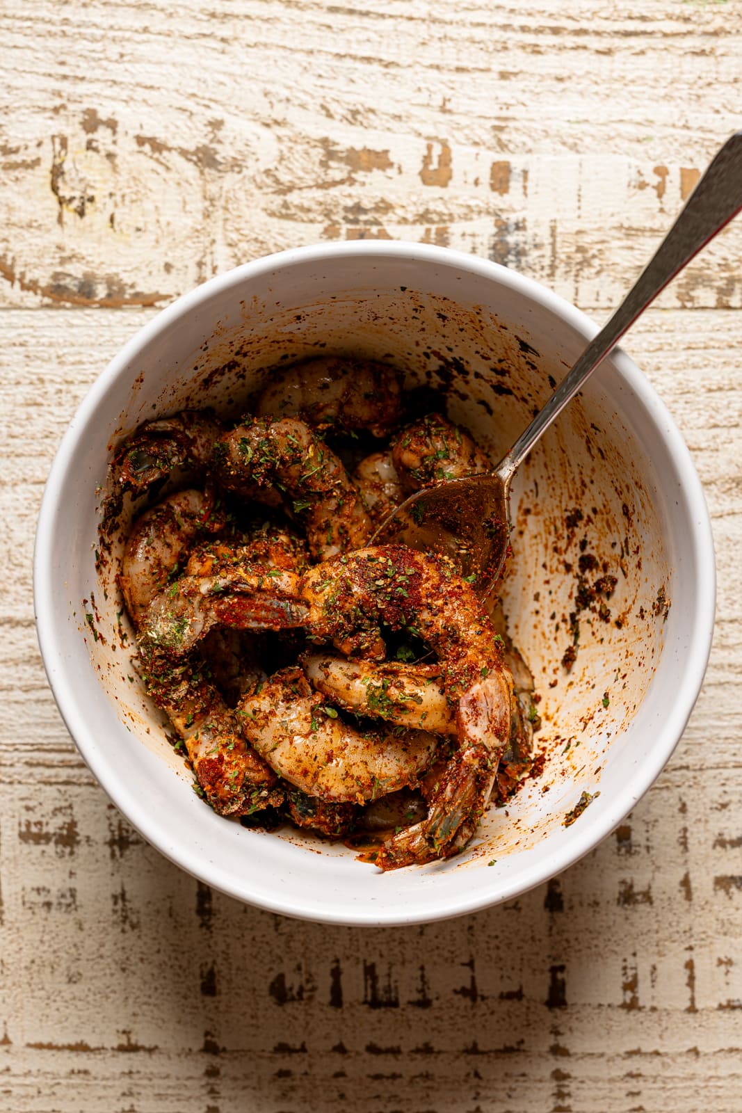 Marinated shrimp in a white bowl with a spoon.