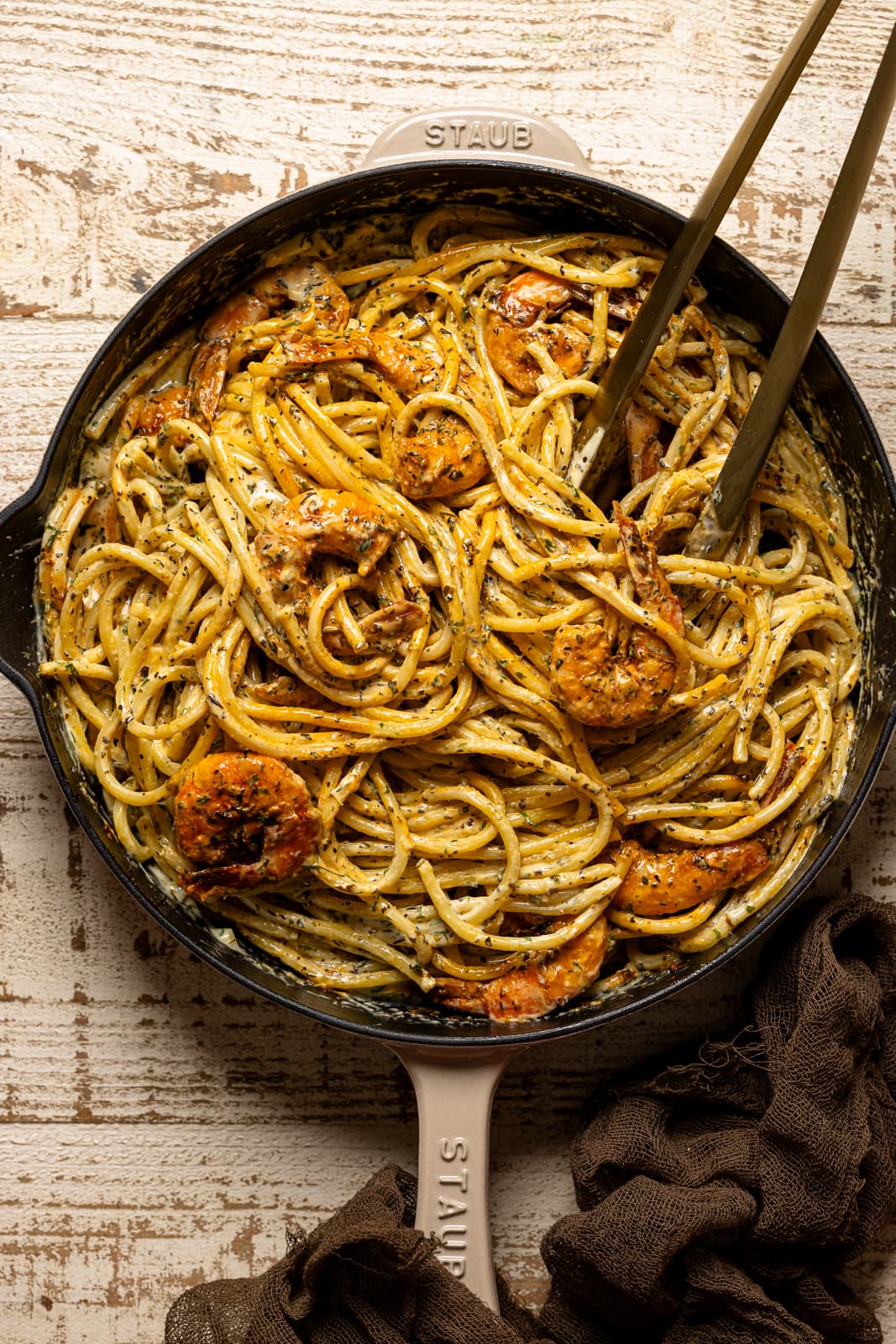 Shrimp pasta in a beige skillet with tongs.