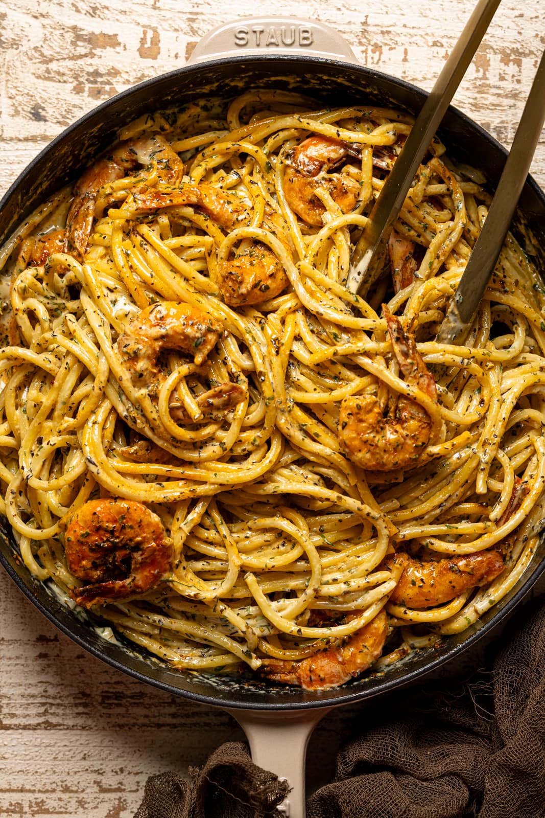 Up close shot of shrimp pasta in skillet with tongs.