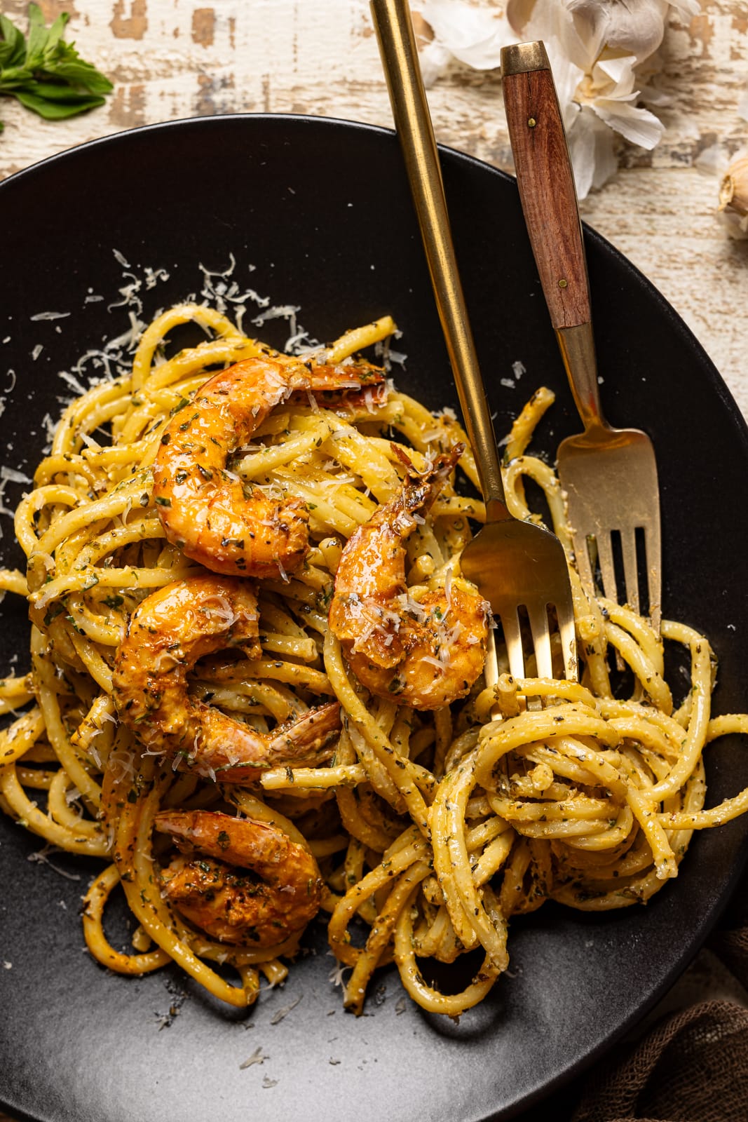 Up close shot of shrimp alfredo pasta in a black plate with two forks.