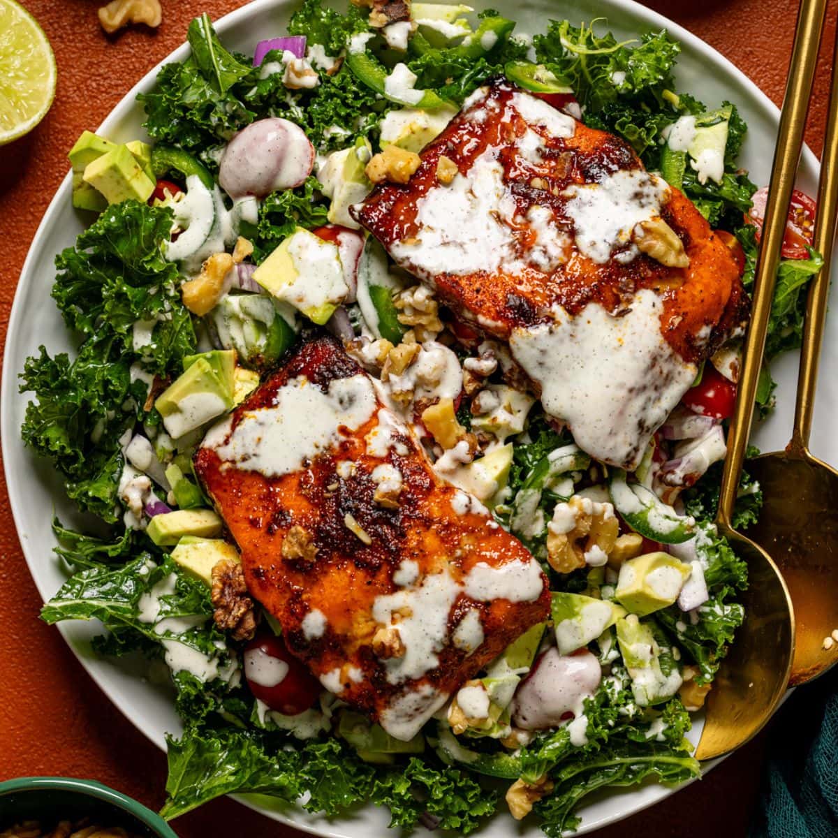 Salad in a platter with two serving utensils and dressing.