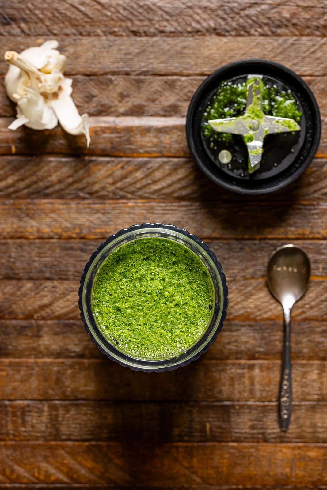 Blended greens in a blender with a spoon on a brown wood table.