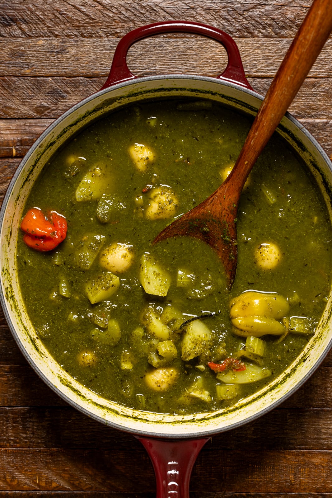 Soup in a burgundy pot with a wooden spoon.