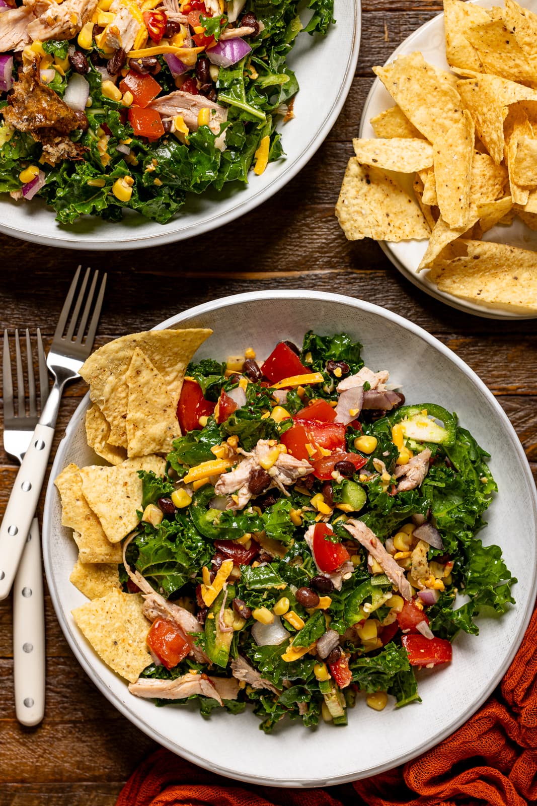 Two bowls of salad with forks and a side of tortilla chips.
