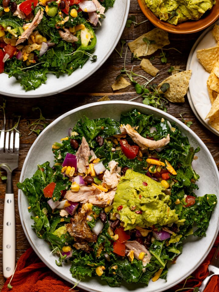 Two bowls of salad with forks, guacamole, and tortilla chips.