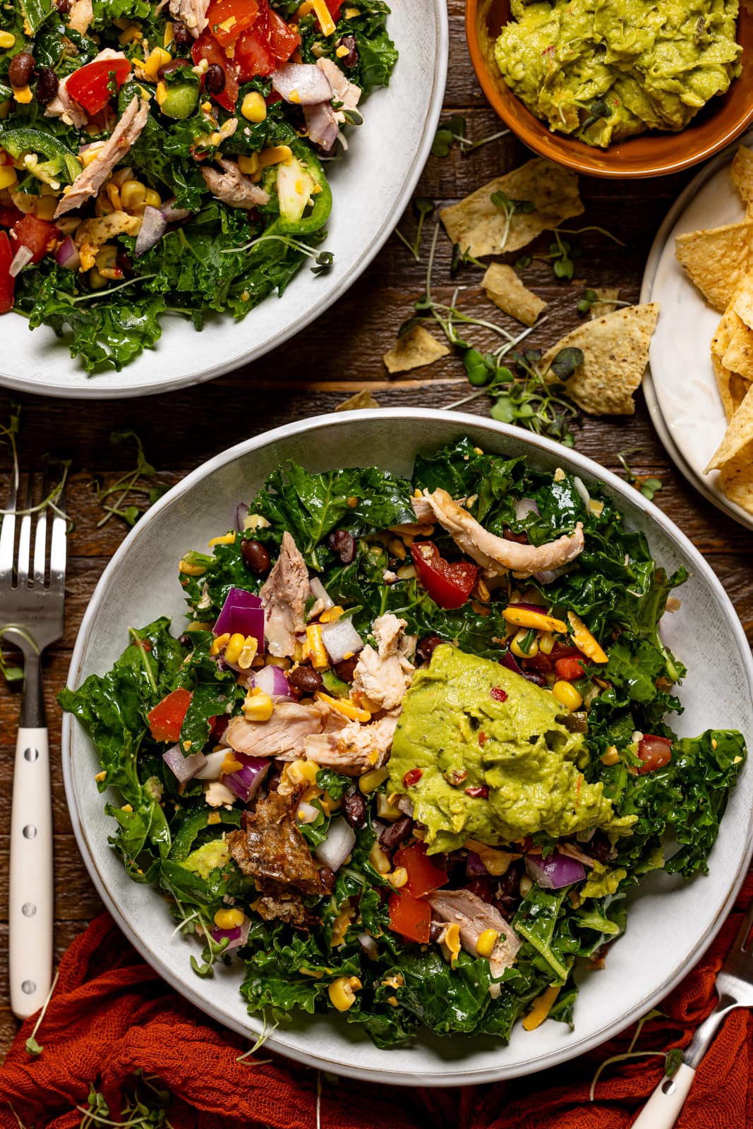 Two bowls of salad with forks, guacamole, and tortilla chips.