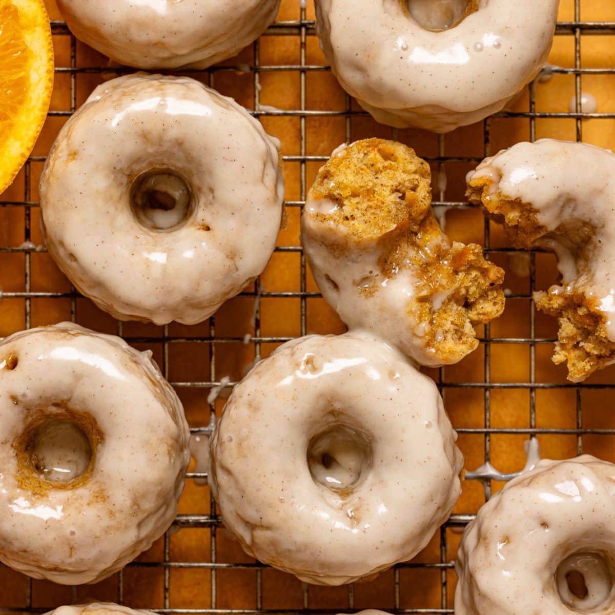 Up close donuts on a wire rack with oranges.