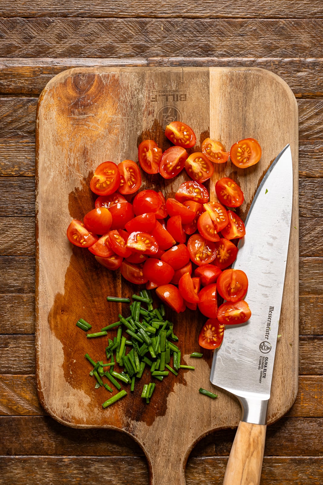 Chopped tomatoes and chives on a cutting board with a knife.