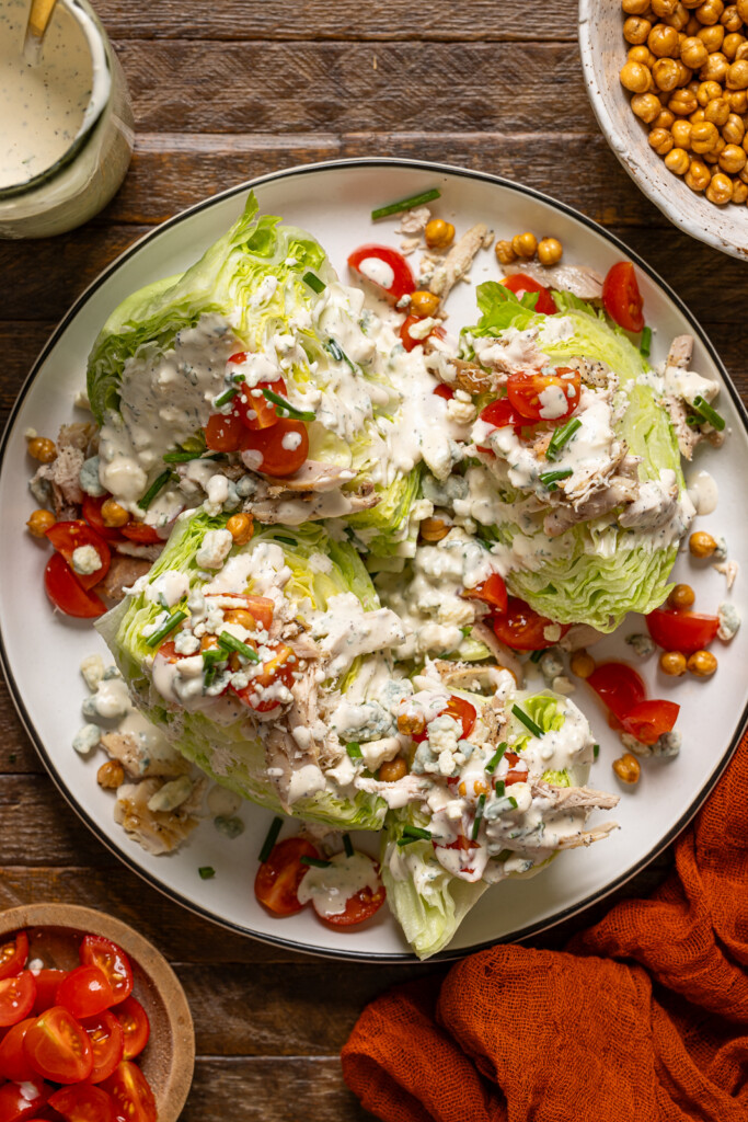 Overhead shot of wedge salads with ingredients on a brown wood table.