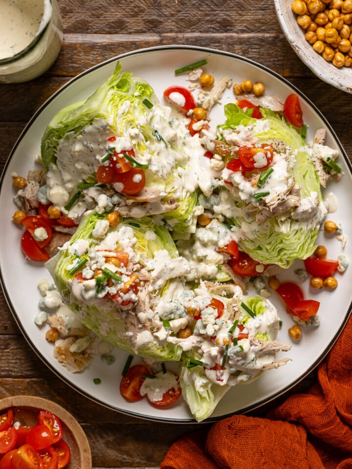 Overhead shot of wedge salads with ingredients on a brown wood table.