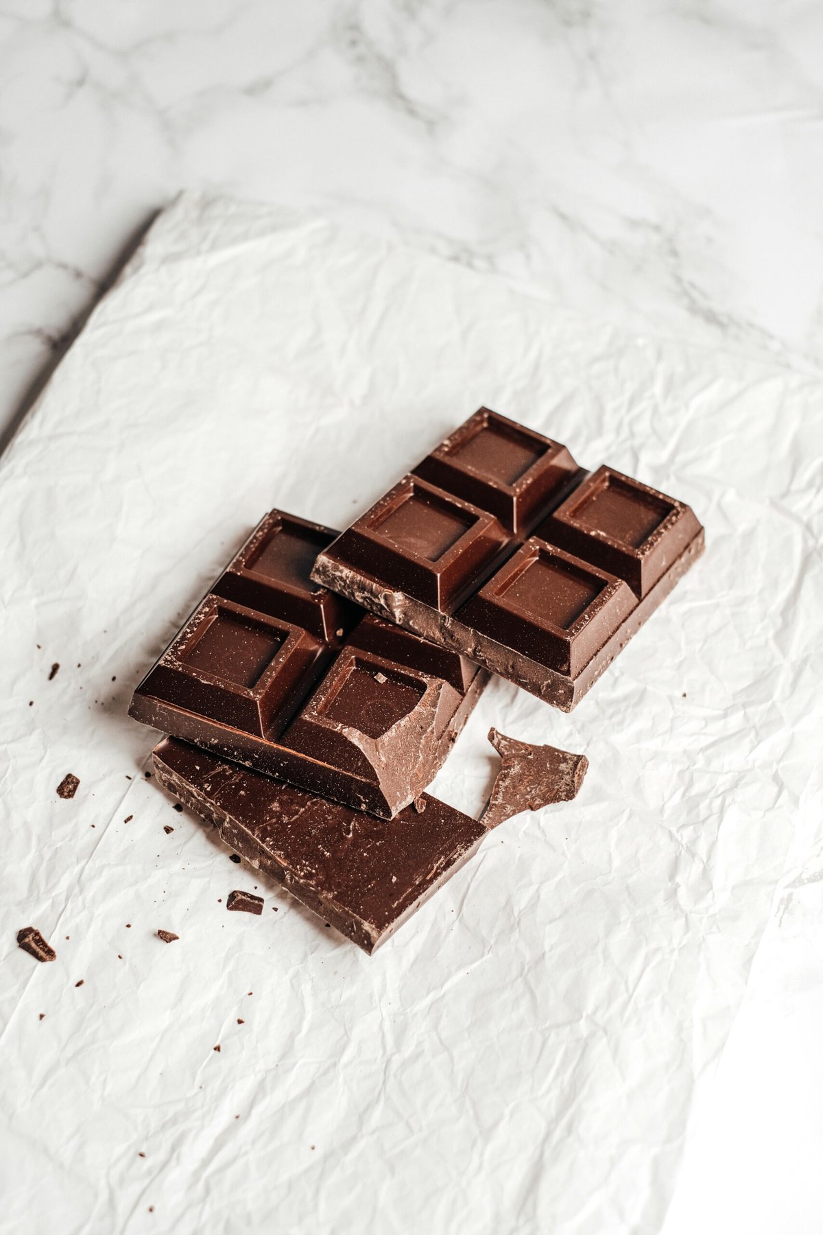 Chocolate bar broken up on a white parchment paper.