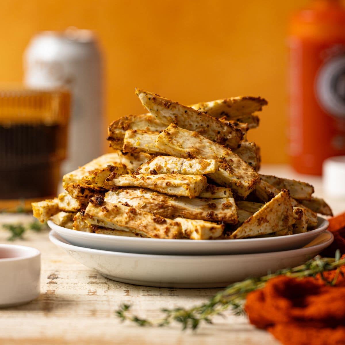 Stacked fries on a white plate with drinks and hot sauce.