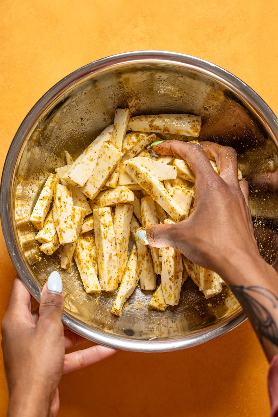 Fries being seasoned in a silver bowl.