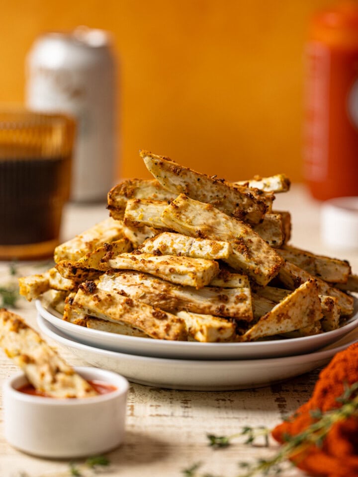Up close shot of Yucca fries stacked on a white plates with a side of dip, drink, and hot sauce.