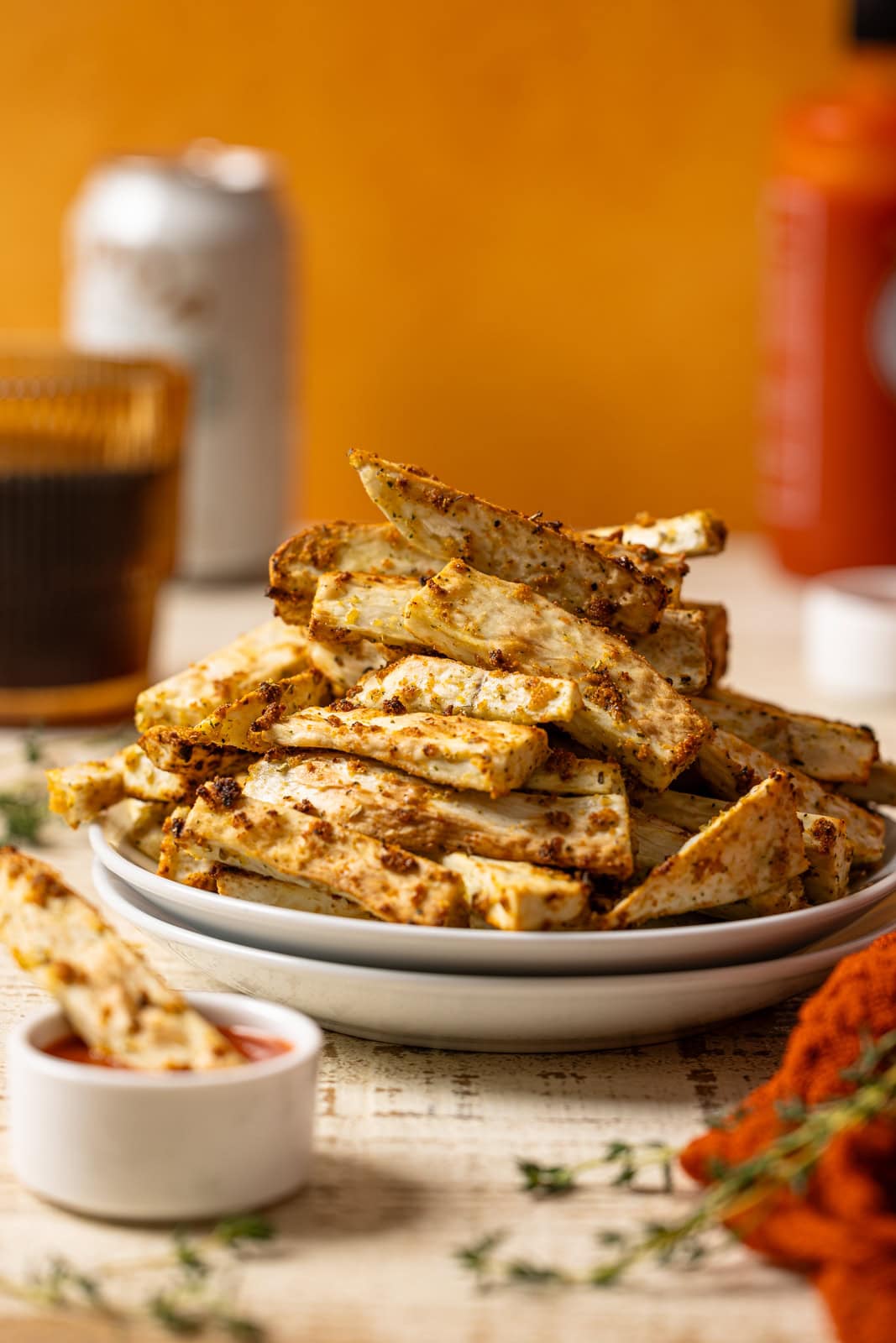 Up close shot of Yucca fries stacked on a white plates with a side of dip, drink, and hot sauce.