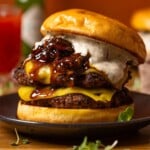 Burger on a black plate with a drink in the background.