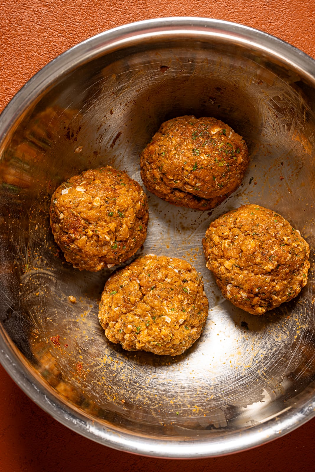 Four burger patties formed in a silver bowl.