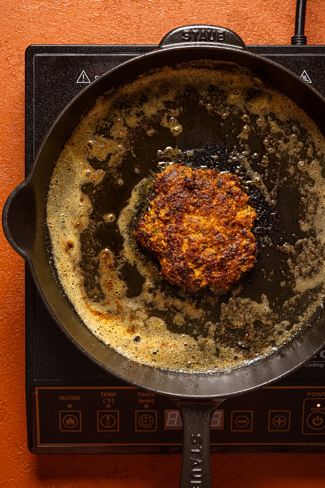 Seared turkey burger patty in a skillet over heat.