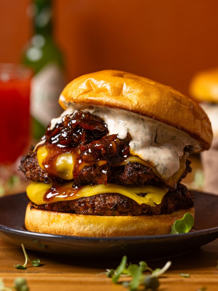 Burger on a black plate with a drink in the background.