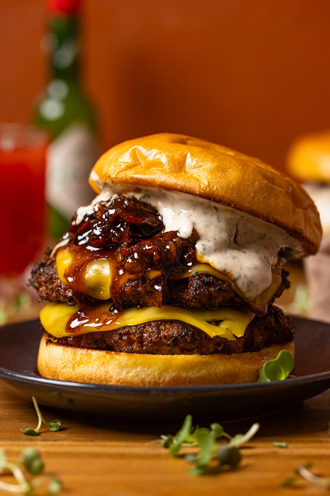 Burger on a black plate with a drink in the background.