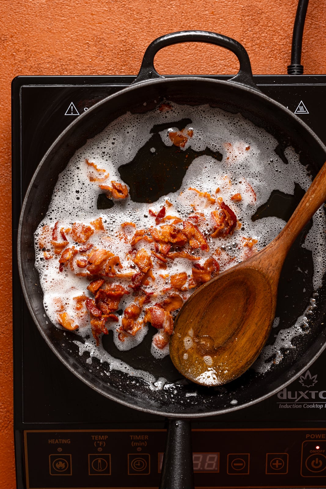 Fried bacon in a skillet with a wooden spoon.