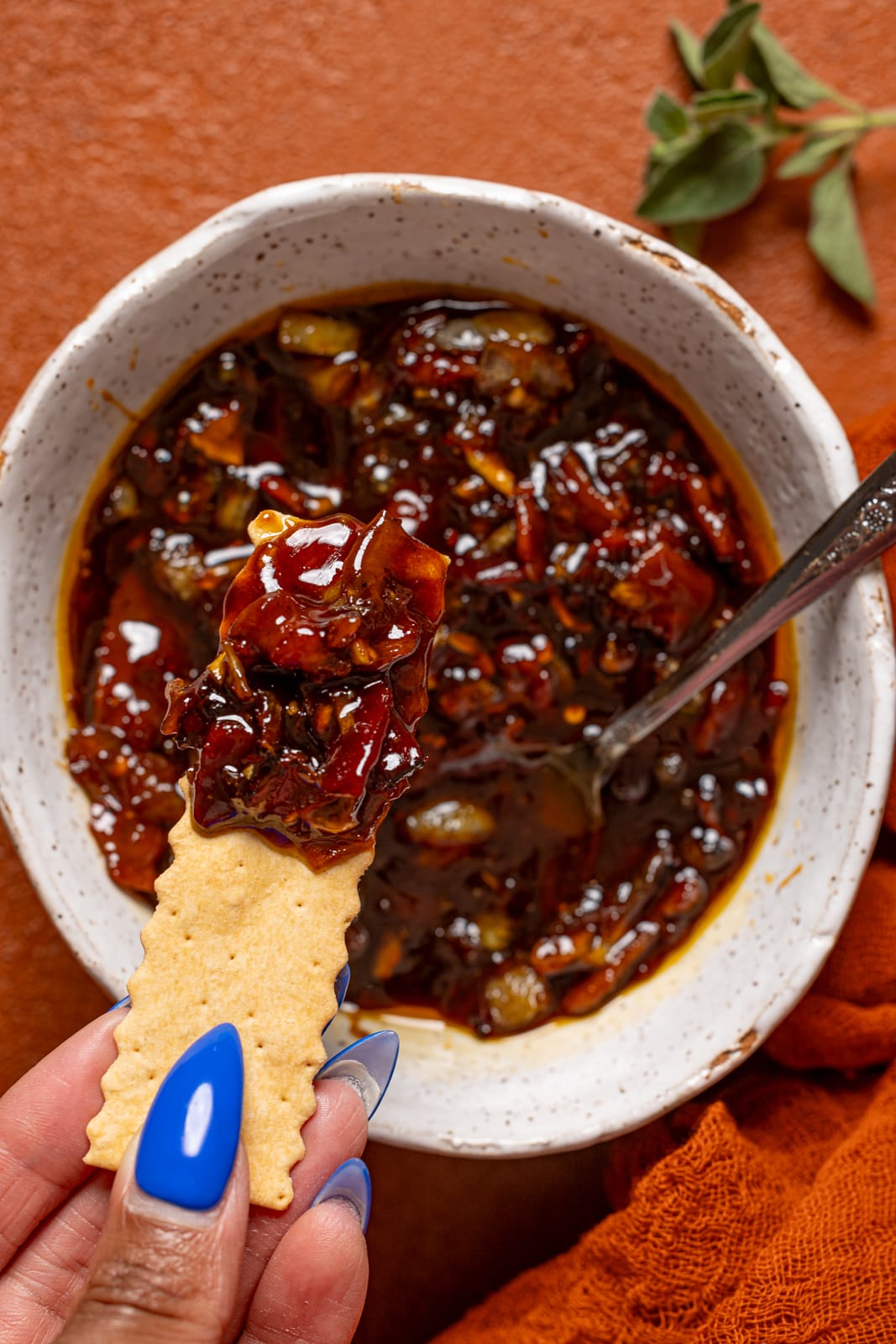 Up close shot of bacon jam in a bowl with a cracker being held.