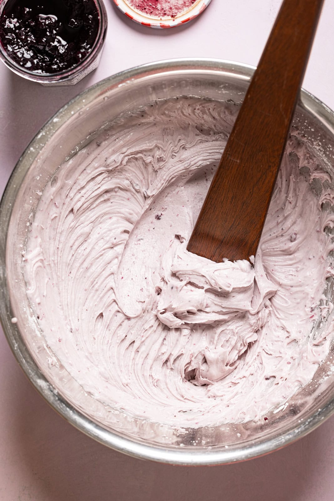 Blueberry frosting in a silver bowl with a wooden spatula. 