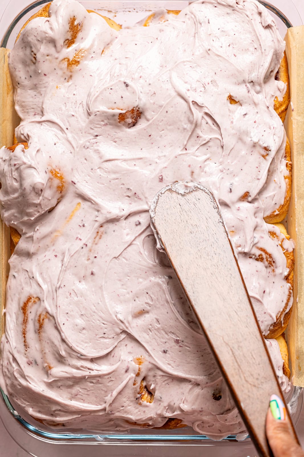 Cinnamon rolls being frosted with wooden spatula. 