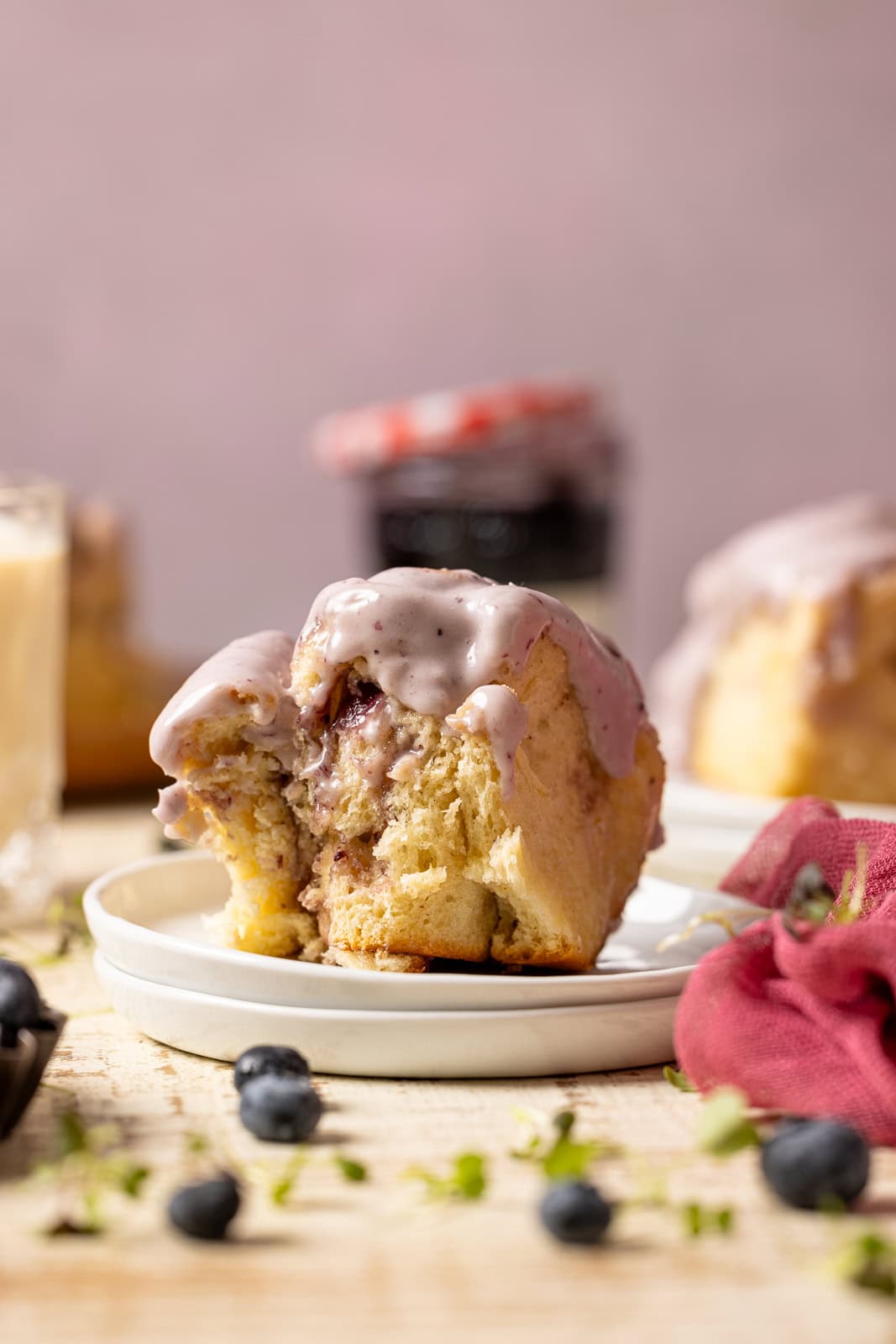 Slice of cinnamon rolls on white plates with jam and blueberries.