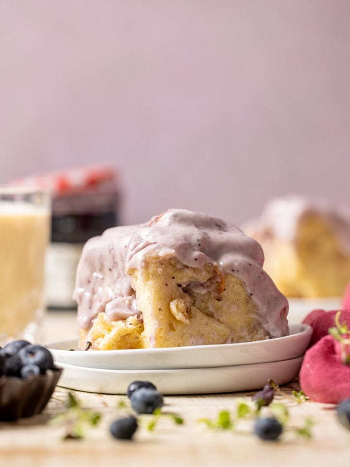 Cinnamon rolls on a stack of plates with a glass of milk, jam, and blueberries.