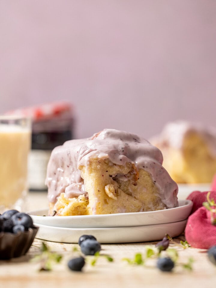 Cinnamon rolls on a stack of plates with a glass of milk, jam, and blueberries.