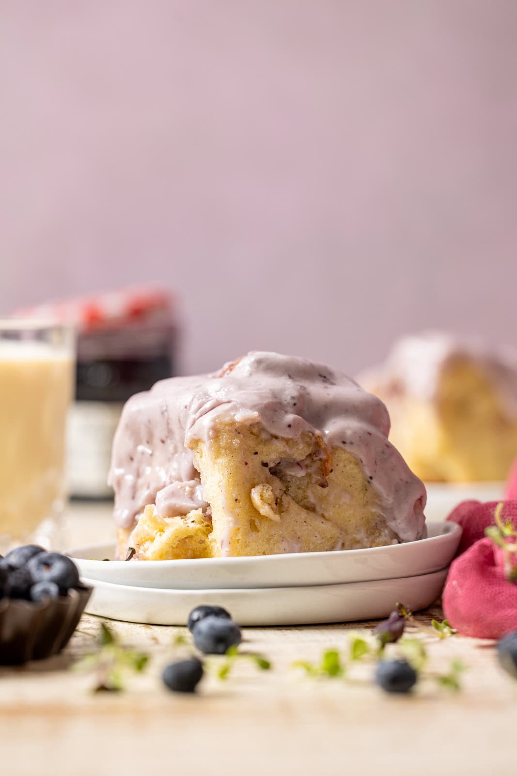 Cinnamon rolls on a stack of plates with a glass of milk, jam, and blueberries.