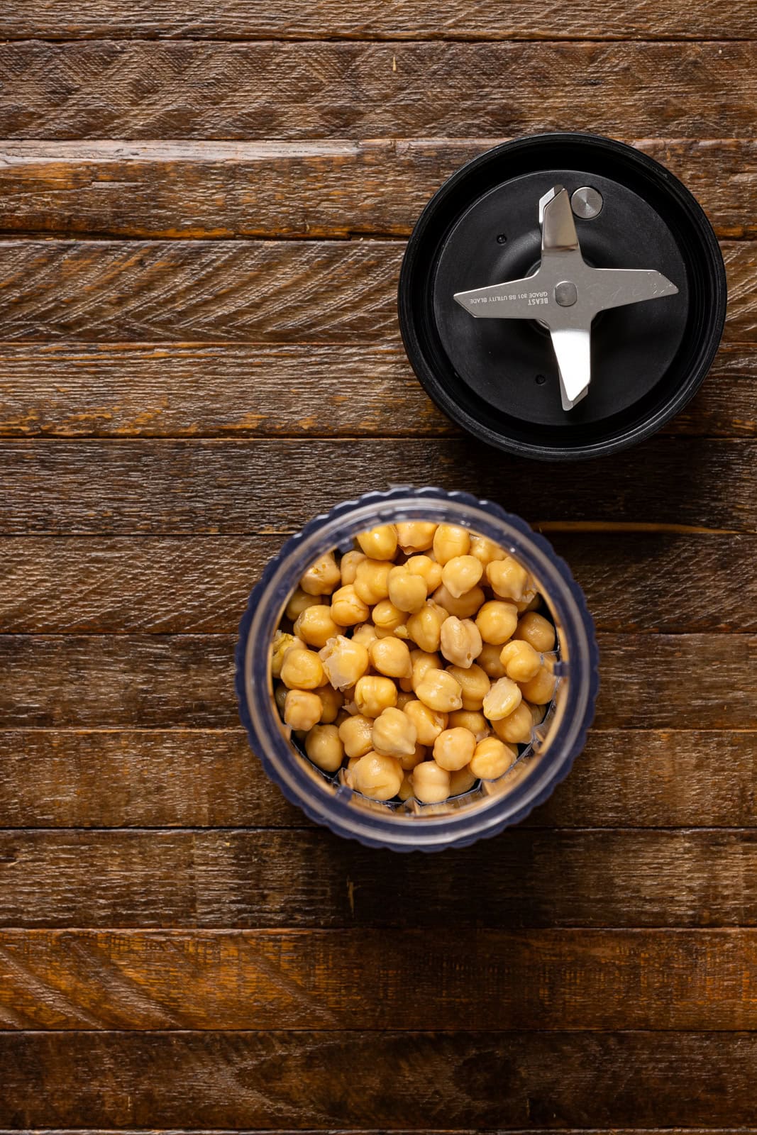 Chickpeas and ingredients in a blender on a brown wood table.