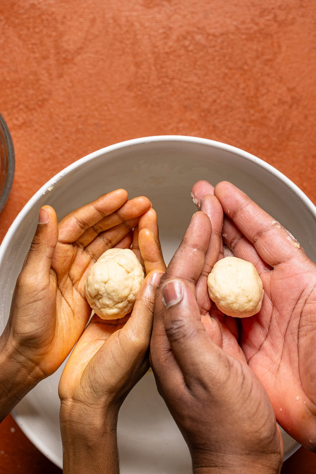 Dough being rolled in hands over a white bowl.