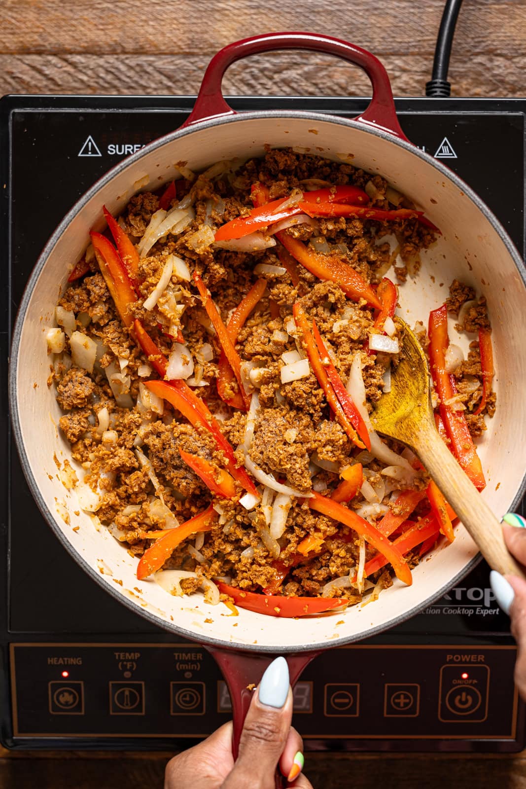 Cooked plant-based meat crumble and veggies in a pot being stirred with a spoon.