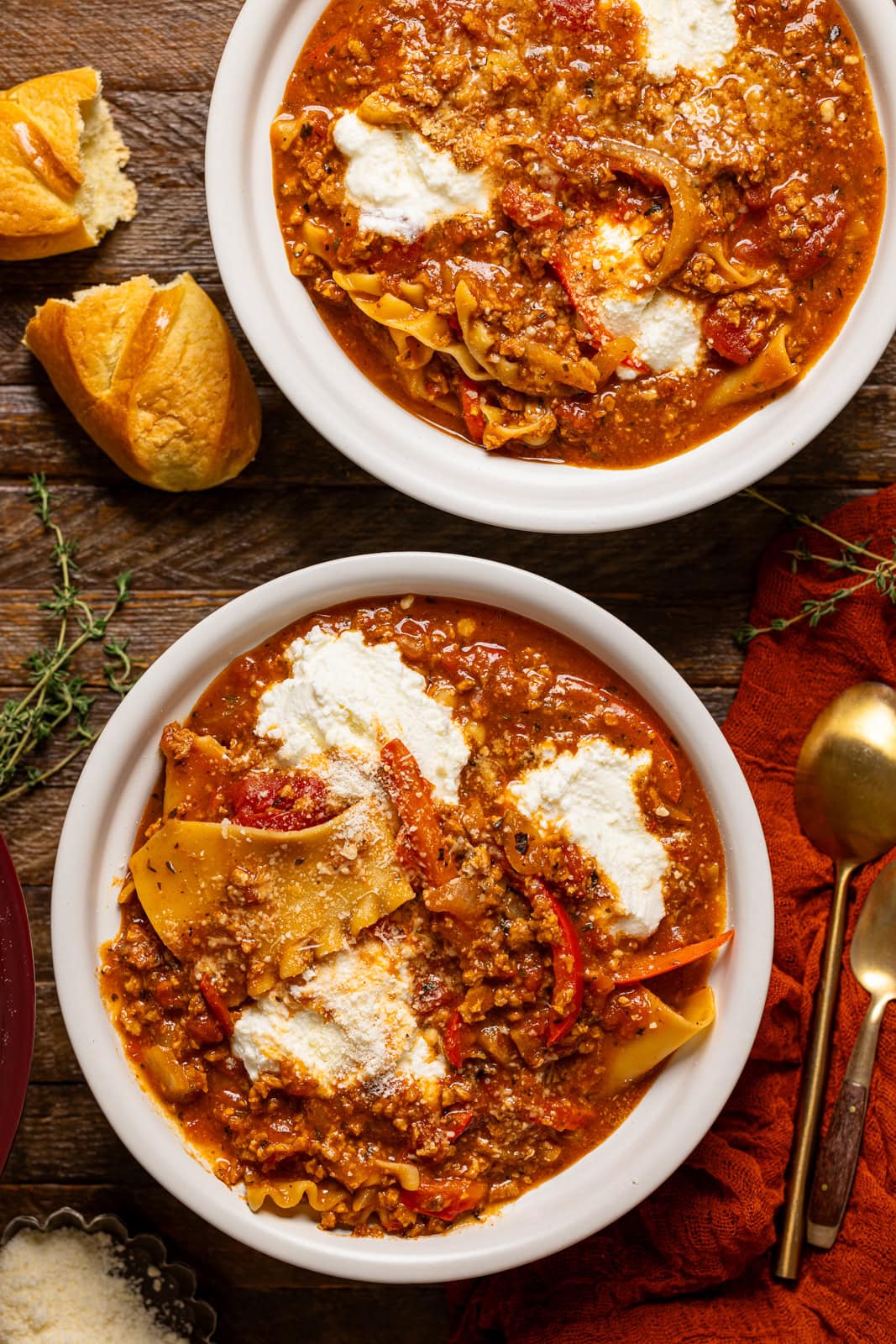 Two bowls of lasagna soup with a spoon and side of bread.