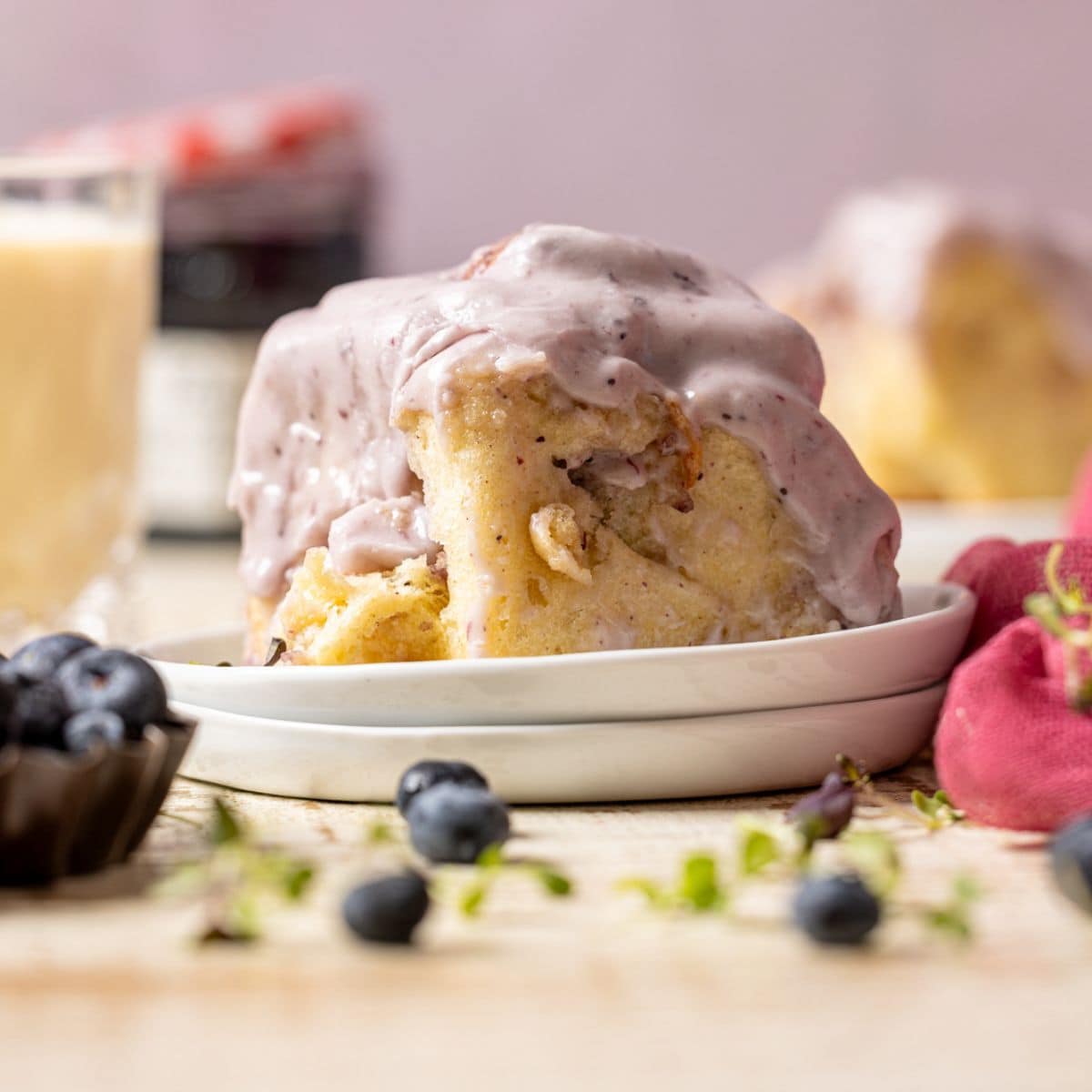 Cinnamon rolls on a stack of plates with a glass of milk, jam, and blueberries.