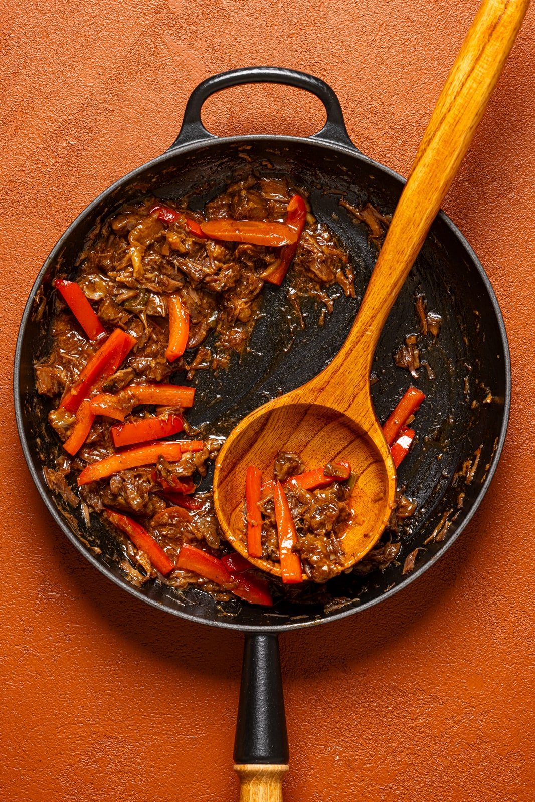 Sautéed oxtail and peppers in a black skillet with a wooden spoon.