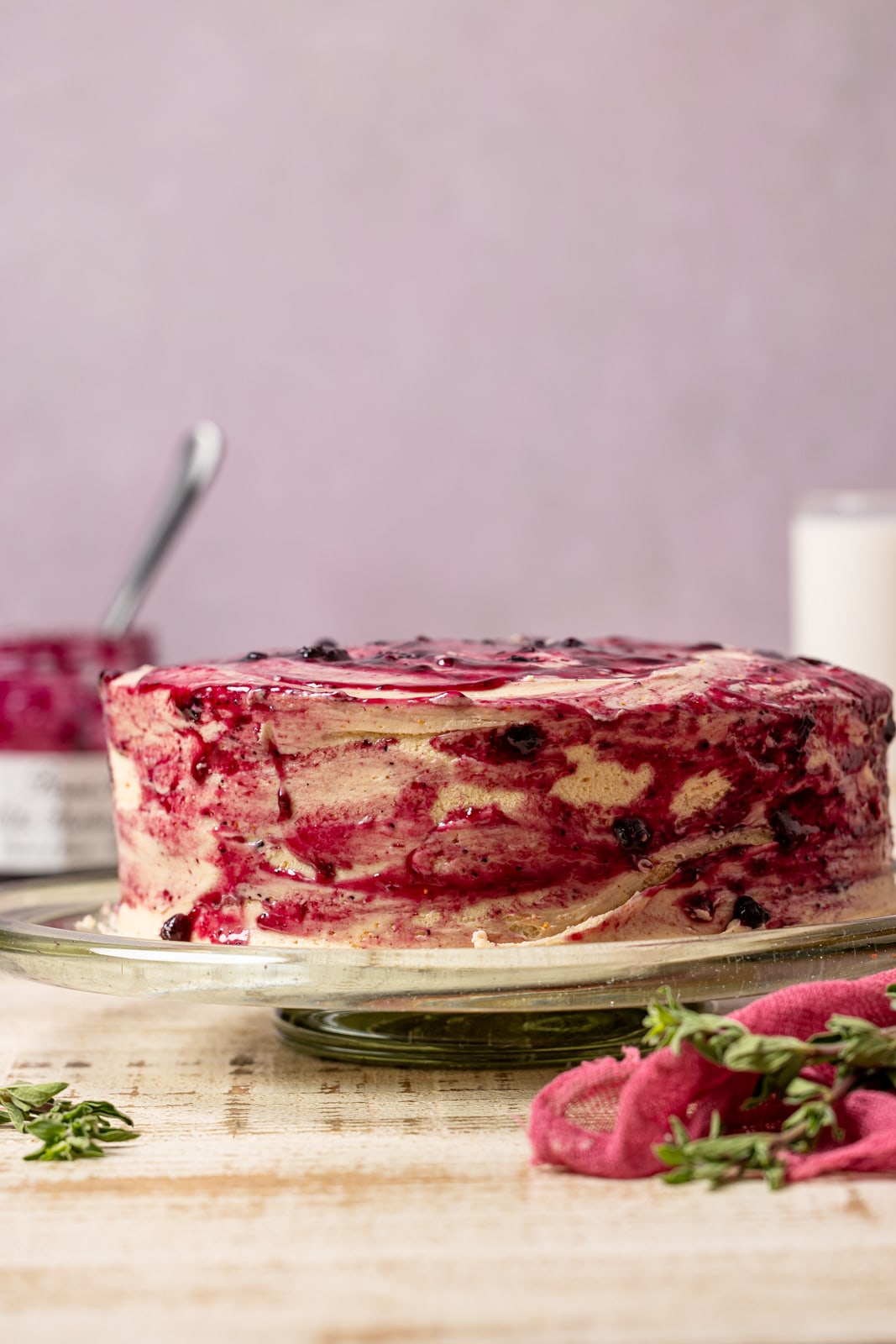 Peanut butter and jelly cake on a cake stand with milk and jam in the background. 