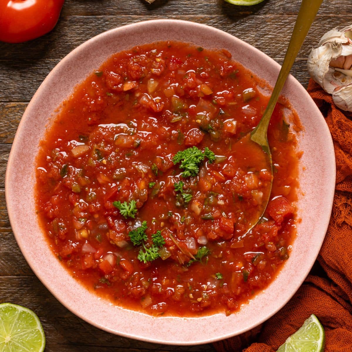 Bowl of salsa with a spoon on a wood table.