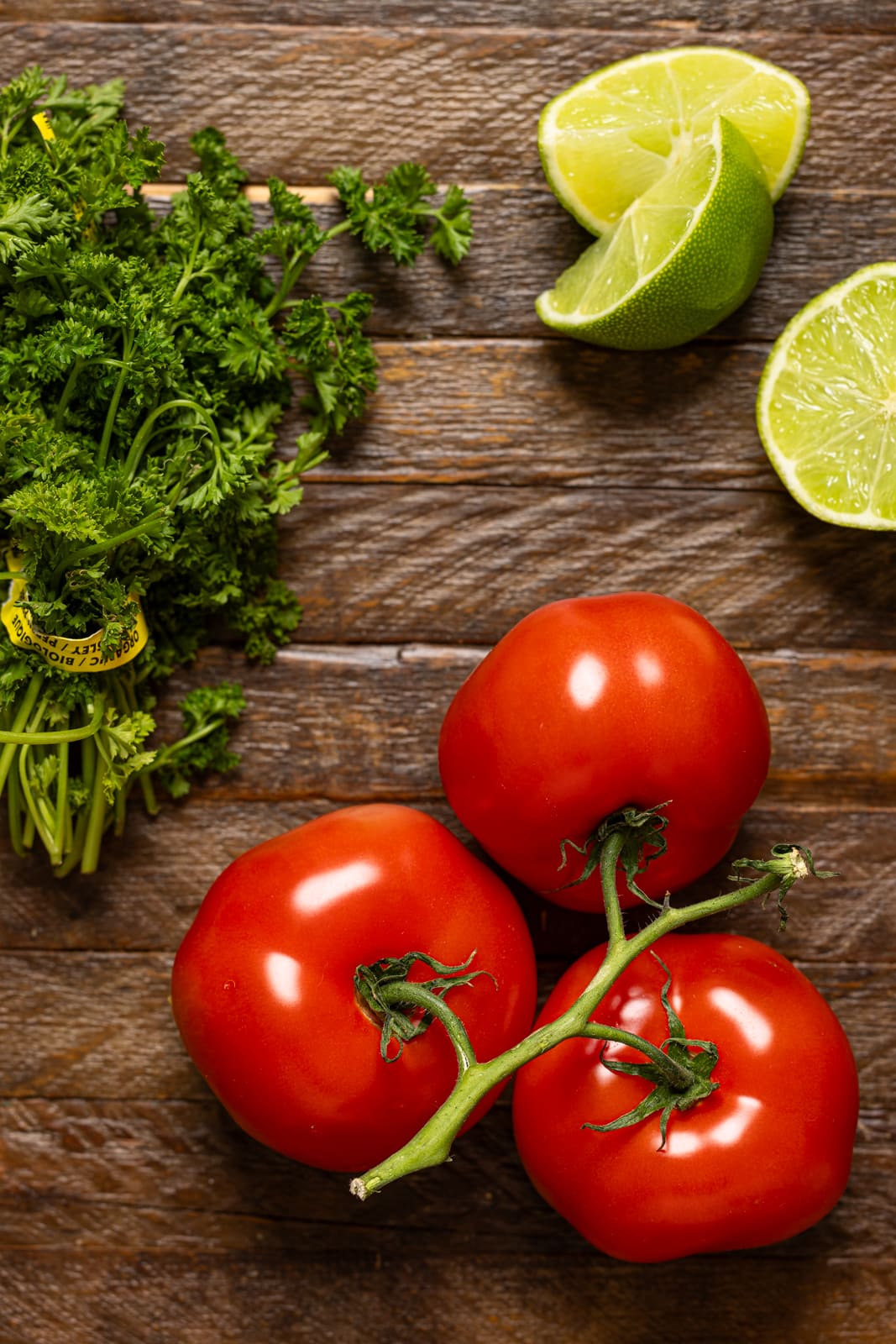 Tomatoes, cilantro, and lime on a brown wood table.